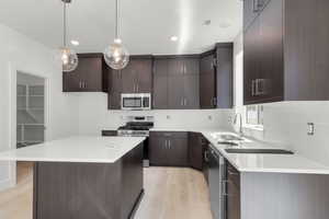Kitchen featuring appliances with stainless steel finishes, light wood-style flooring, light countertops, dark brown cabinetry, and decorative light fixtures