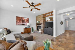 Living area with a ceiling fan, a stone fireplace, stone finish flooring, and recessed lighting