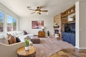 Living area with ceiling fan, a stone fireplace, and a textured ceiling
