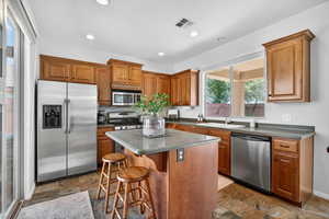Kitchen with stainless steel appliances, dark stone finish flooring, a kitchen island, brown cabinets, and recessed lighting
