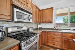 Kitchen with stainless steel appliances, brown cabinetry, dark countertops, and decorative backsplash