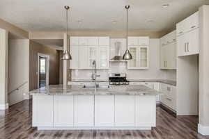 Kitchen featuring backsplash, wall chimney range hood, a center island with sink, gas range, and white cabinetry