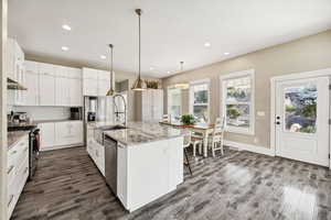 Kitchen with white cabinetry, tasteful backsplash, stainless steel appliances, hanging light fixtures, and light stone counters