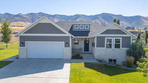 Craftsman inspired home featuring stone siding, a front yard, a mountain view, a garage, and driveway