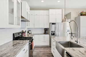Kitchen with stainless steel appliances, glass insert cabinets, white cabinetry, light stone counters, and recessed lighting