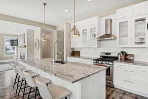 Kitchen featuring white cabinetry, stainless steel gas range oven, light stone counters, glass insert cabinets, and recessed lighting