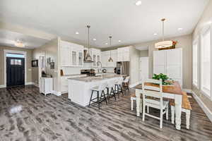 Kitchen with tasteful backsplash, a breakfast bar area, white cabinets, an island with sink, and light stone counters