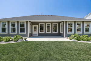 Rear view of property with a shingled roof, a lawn, and a patio