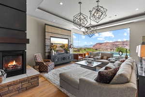 Living room with wood finished floors, a tray ceiling, a glass covered fireplace, a mountain view, and a chandelier