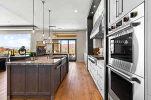 Kitchen with appliances with stainless steel finishes, light wood-style floors, an island with sink, dark brown cabinets, and light stone countertops