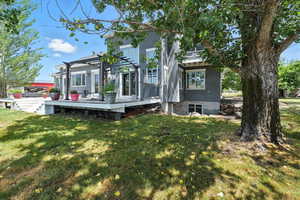 Back of house with a deck, a pergola, stucco siding, and a lawn
