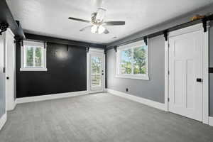 Unfurnished bedroom featuring a textured ceiling, access to exterior, light colored carpet, a barn door, and a ceiling fan