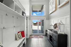 Mudroom featuring dark tile patterned floors, a decorative wall, a towering ceiling, and a wainscoted wall