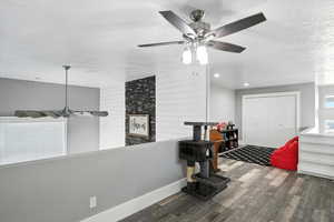 Loft entrance with ceiling fan, a textured ceiling, wood finished floors, and wooden walls