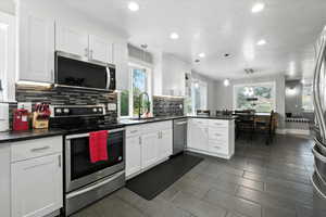 Kitchen with appliances with stainless steel finishes, a peninsula, tasteful backsplash, dark countertops, and white cabinets