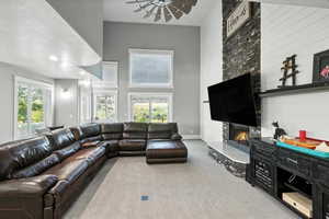 Carpeted living room featuring a large fireplace, healthy amount of natural light, a high ceiling, and a ceiling fan