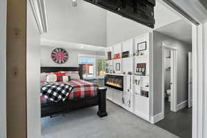 Bedroom featuring a glass covered fireplace, carpet flooring, a high ceiling, and ensuite bath