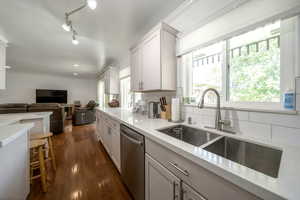 Kitchen with dark wood-style floors, stainless steel dishwasher, crown molding, light countertops, and decorative backsplash