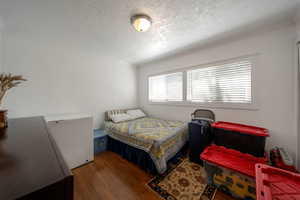Bedroom with wood finished floors, a textured ceiling, white refrigerator, and crown molding