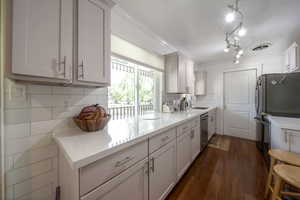 Kitchen featuring dark wood-style floors, crown molding, appliances with stainless steel finishes, decorative backsplash, and white cabinets