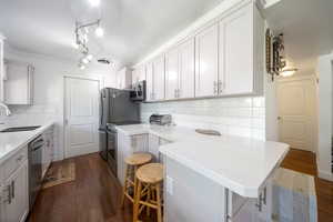 Kitchen with a breakfast bar, decorative backsplash, dark wood finished floors, a peninsula, and crown molding
