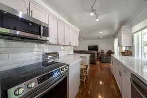 Kitchen with backsplash, appliances with stainless steel finishes, dark wood-style floors, white cabinetry, and ornamental molding