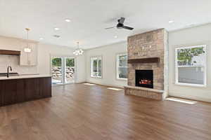Unfurnished living room with wood finished floors, a stone fireplace, a ceiling fan, a chandelier, and recessed lighting
