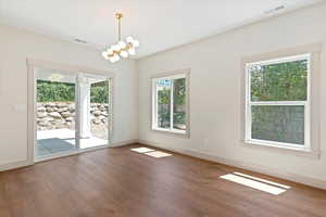 Unfurnished dining area with healthy amount of natural light, wood finished floors, and a chandelier