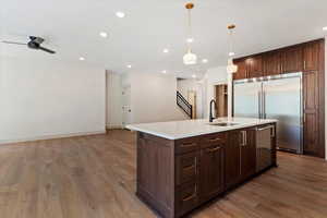 Kitchen featuring appliances with stainless steel finishes, an island with sink, wood finished floors, recessed lighting, and hanging light fixtures