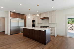 Kitchen with built in appliances, light countertops, custom exhaust hood, wood finished floors, and recessed lighting