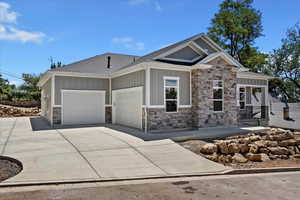 View of front facade featuring board and batten siding, stone siding, driveway, roof with shingles, and a garage