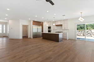 Kitchen with built in appliances, wood finished floors, light countertops, an island with sink, and recessed lighting