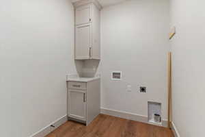 Laundry area with hookup for an electric dryer, hookup for a washing machine, light wood-style floors, and cabinet space