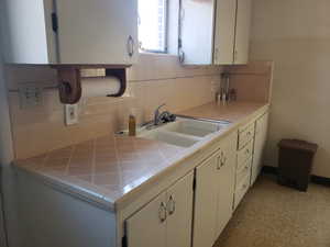 Kitchen featuring tile counters, tasteful backsplash, white cabinetry, and light floors