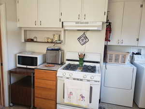 Kitchen featuring white range with gas cooktop, separate washer and dryer, under cabinet range hood, light countertops, and white cabinetry