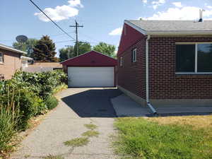 View of home's exterior featuring brick siding, a detached garage, an outbuilding, and roof with shingles