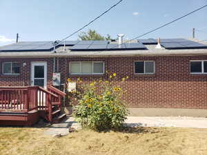 Back of house featuring brick siding, roof mounted solar panels, and a shingled roof