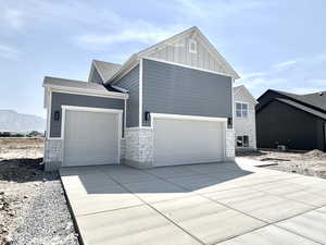 View of front of property with stone siding, board and batten siding, driveway, and an attached garage