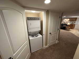 Laundry room featuring stacked washer and dryer, light colored carpet, and a textured ceiling