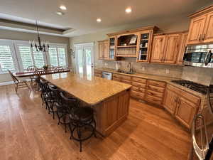 Kitchen with a tray ceiling, a chandelier, stainless steel appliances, a breakfast bar, and decorative backsplash