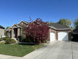View of front of property featuring a garage, a front lawn, concrete driveway, roof with shingles, and brick siding