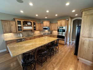 Kitchen with arched walkways, a breakfast bar area, appliances with stainless steel finishes, a kitchen island, and light stone countertops