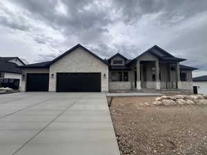 View of front of property with board and batten siding, a garage, a porch, stone siding, and driveway