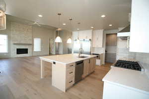 Kitchen with light wood-type flooring, ceiling fan, a stone fireplace, appliances with stainless steel finishes, and recessed lighting
