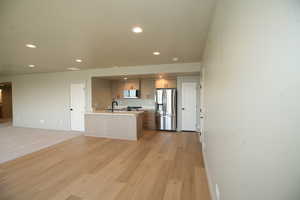 Kitchen with appliances with stainless steel finishes, open floor plan, a kitchen island with sink, recessed lighting, and light wood finished floors. All appliances are included.