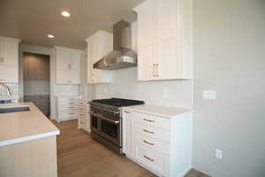 Kitchen with wall chimney exhaust hood, range with two ovens, light wood-type flooring, decorative backsplash, and recessed lighting
