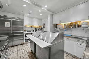 Kitchen with light tile patterned floors, high end appliances, decorative backsplash, white cabinets, and recessed lighting