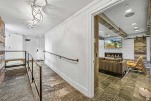 Staircase with stone finish floors, a barn door, a brick fireplace, recessed lighting, and beamed ceiling