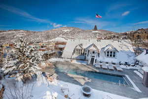 Snow covered back of property featuring a mountain view, a patio area, and a community pool