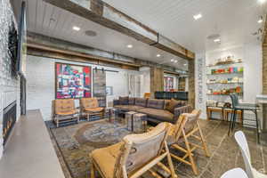Living room featuring a warm lit fireplace, recessed lighting, a barn door, brick wall, and beam ceiling